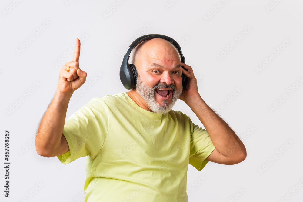 Fototapeta premium Senior elderly retired Indian asian man wears headphone and listening to music and dancing on beats against white background