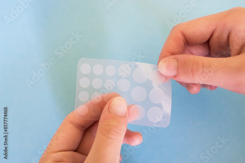 Close-up round acne patch on finger on blue background. Acne patches for treatment of pimple and rosacea close-up.