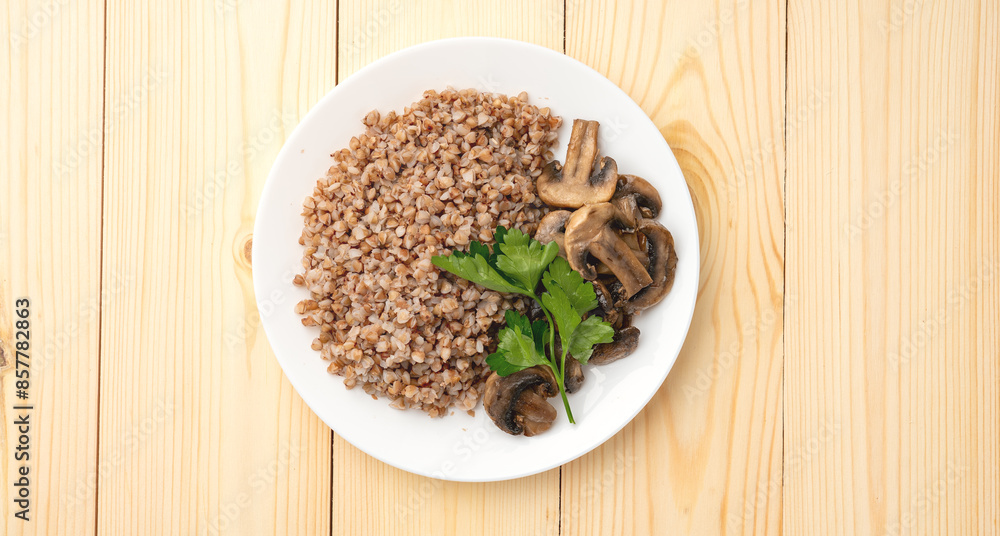 Buckwheat porridge with fried mushrooms on a plate on a wooden background. A green leaf decorates the dish. Healthy diet food. The concept of healthy eating. Buckwheat porridge with fried mushrooms on a plate on a wooden background. A green leaf decorates the dish. Healthy diet food. The concept of healthy eating.