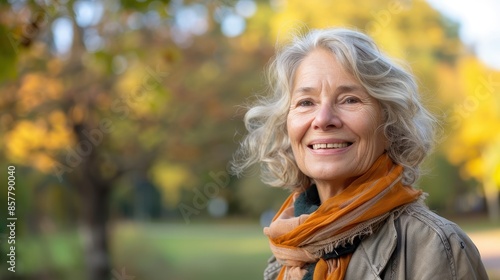 A senior woman smiles while wearing a scarf in an autumn park © Sasa Visual