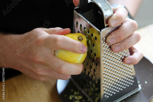 A white man grating lemon zest with a grater. Preparing food. Refreshing ingredients for cooking and baking. Closeup color image of the lemon, grater and the hand of the man. Healthy lifestyle image.