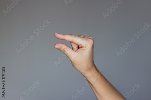 Female hand making a gesture like holding something tiny with two fingers or measuring and showing small size isolated on a dark gray background. Mockup with empty copy space for a intended object photo