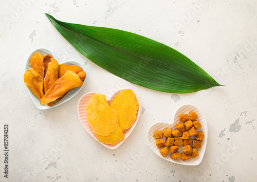 Dried mango slices and balls in heart shaped plates on light background.