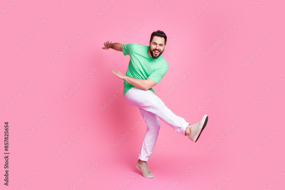 Full size photo of ecstatic good mood guy dressed green t-shirt white trousers dancing on one leg isolated on pink color background Full size photo of ecstatic good mood guy dressed green t-shirt white trousers dancing on one leg isolated on pink color background