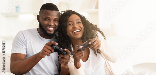 A couple smiles and laughs together while playing video games in their living room. photo