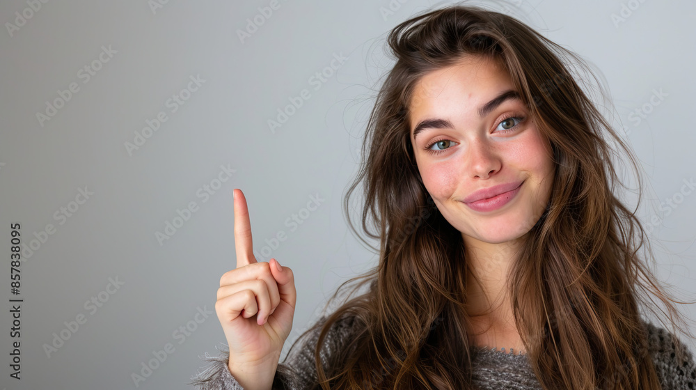 Caucasian Woman Pointing Up with a Slight Smile in Front of a Gray Background Caucasian Woman Pointing Up with a Slight Smile in Front of a Gray Background