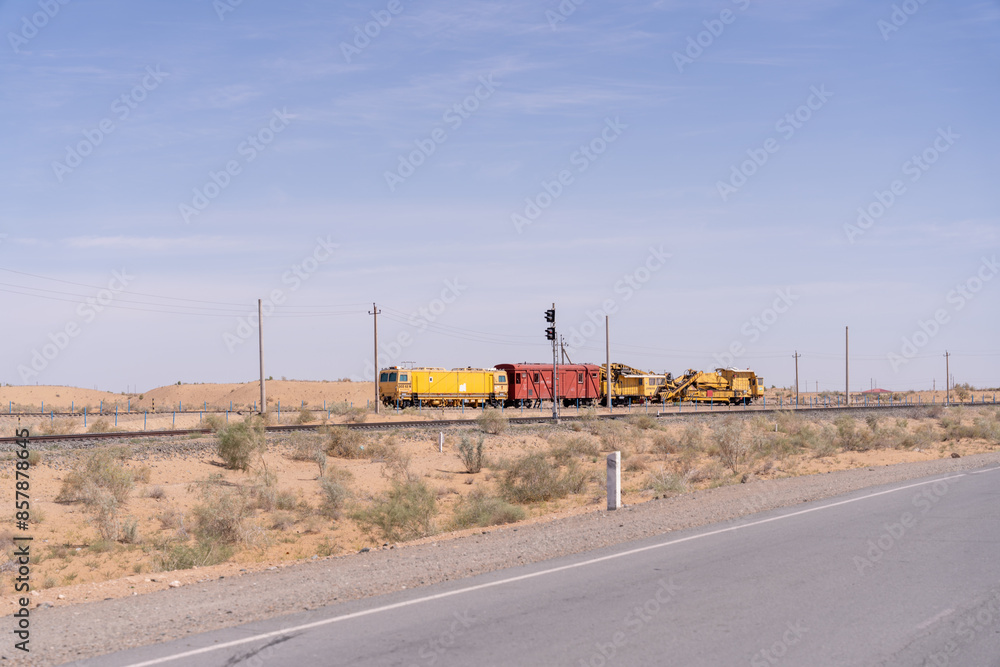 A train is traveling down a track in a desert. The train is yellow and red. The desert is dry and barren A train is traveling down a track in a desert. The train is yellow and red. The desert is dry and barren