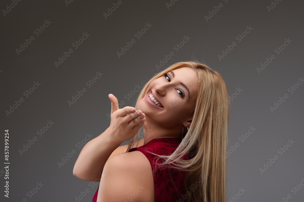Young woman pointing with finger while smiling on gray backgroun Young woman pointing with finger while smiling on gray backgroun