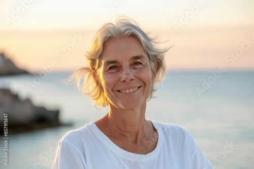 smiling attractive older woman in white tshirt relaxing by the sea serene lifestyle portrait © furyon