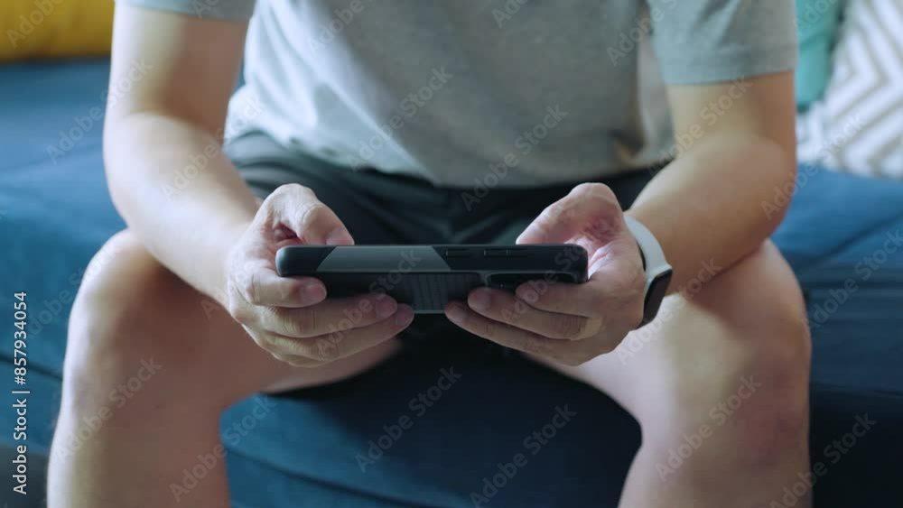 A man sitting on a sofa playing games on his phone A man sitting on a sofa playing games on his phone