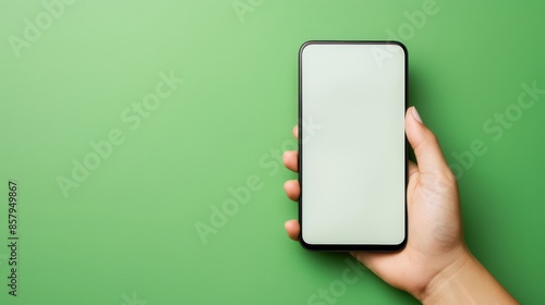 Hand with mobile phone mockup screen on a green background, copy space