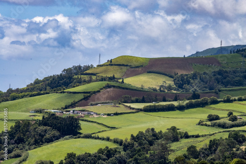Azores panorama in Ponta Delgada, naturalistic landscape with deep green fields and blue sky. Scenic view of rolling green hills with a clear blue sky and a few scattered clouds on a sunny day