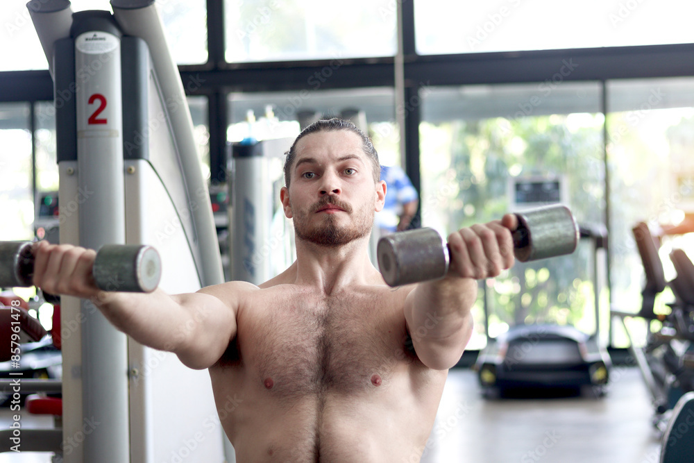 Strong young muscular man lifting dumbbell at gym. Handsome sport man doing weightlifting exercise at fitness. Athletic workout weight training, doing bodybuilding program for healthy and perfect body Strong young muscular man lifting dumbbell at gym. Handsome sport man doing weightlifting exercise at fitness. Athletic workout weight training, doing bodybuilding program for healthy and perfect body
