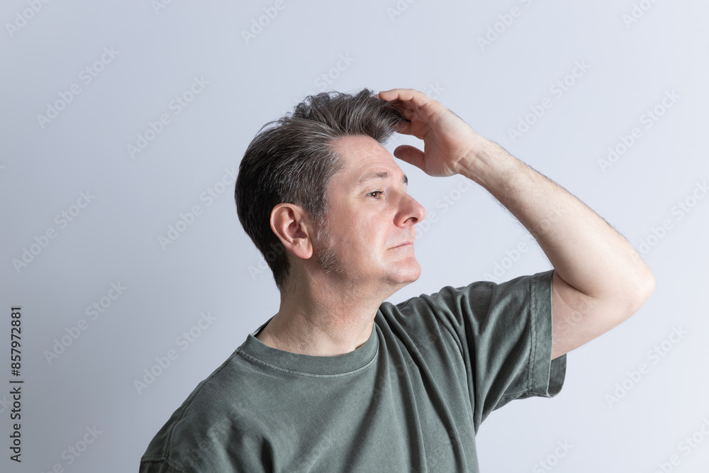 Mature man in his 50's in profile, casually dressed with gray hair styled with a toupee, touching his hair with one hand. Copy Space. Concept of stylish, masculine, stylish hairstyle and hair care Mature man in his 50's in profile, casually dressed with gray hair styled with a toupee, touching his hair with one hand. Copy Space. Concept of stylish, masculine, stylish hairstyle and hair care
