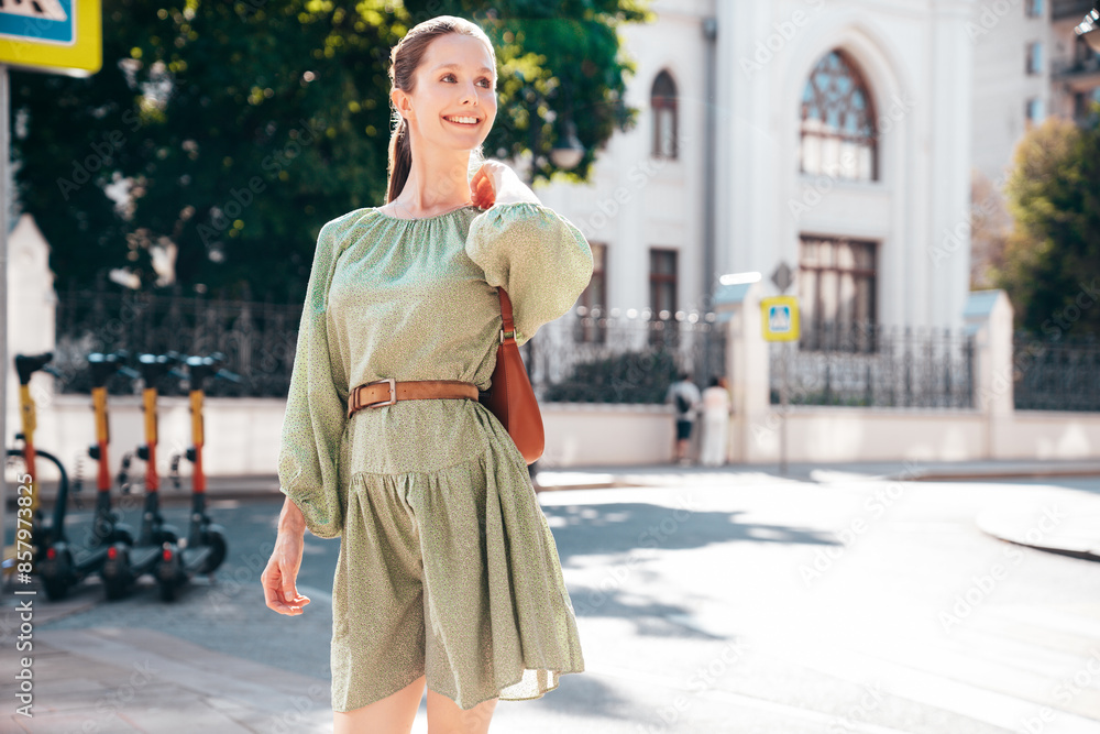 Fototapeta premium Portrait of young beautiful smiling brunette woman in trendy summer dress. Sexy carefree woman posing in street. Positive model outdoors at sunny day. Cheerful and happy. Holds handbag