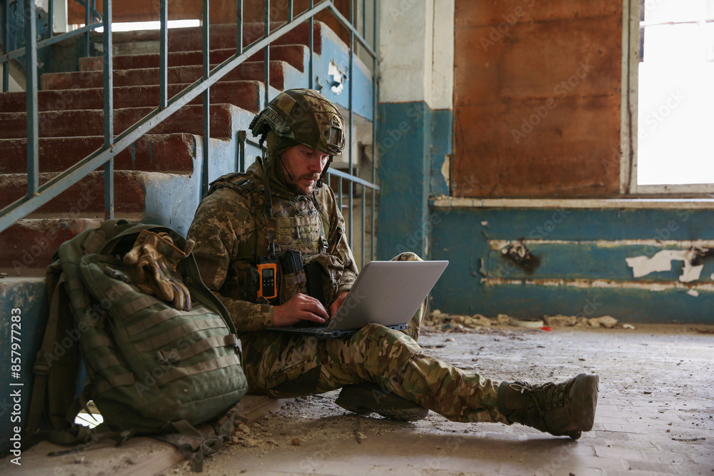 Fototapeta premium Military mission. Soldier in uniform using laptop inside abandoned building
