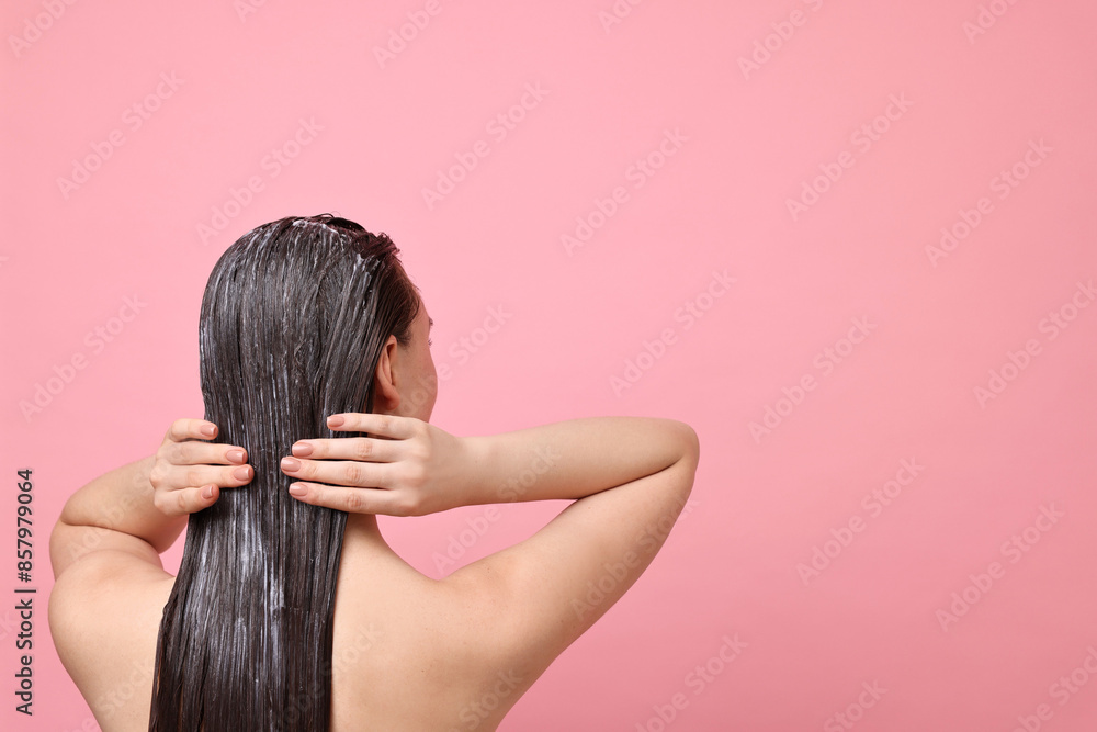 Fototapeta premium Woman applying hair mask on pink background, back view. Space for text