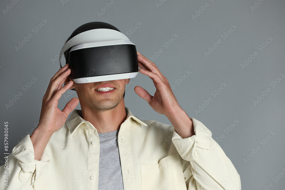Smiling man using virtual reality headset on gray background, space for text Smiling man using virtual reality headset on gray background, space for text