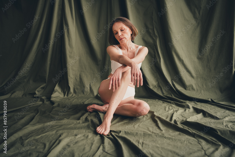 Unretouched photo of old lady sit posing touch look legs knees isolated green color linen background Unretouched photo of old lady sit posing touch look legs knees isolated green color linen background