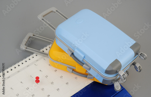 Planning travel and vacation concept. Blue and orange suitcases and calendar with push pin on gray background.	