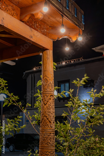 A wooden pole with lights on it is lit up at night. The pole is next to a building with a window