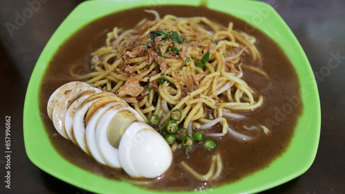 raditional Mie Lendir Noodle Dish from Riau Islands Batam Indonesia served on a green plate with boiled egg slices and garnished with fried shallots and green chilies photo