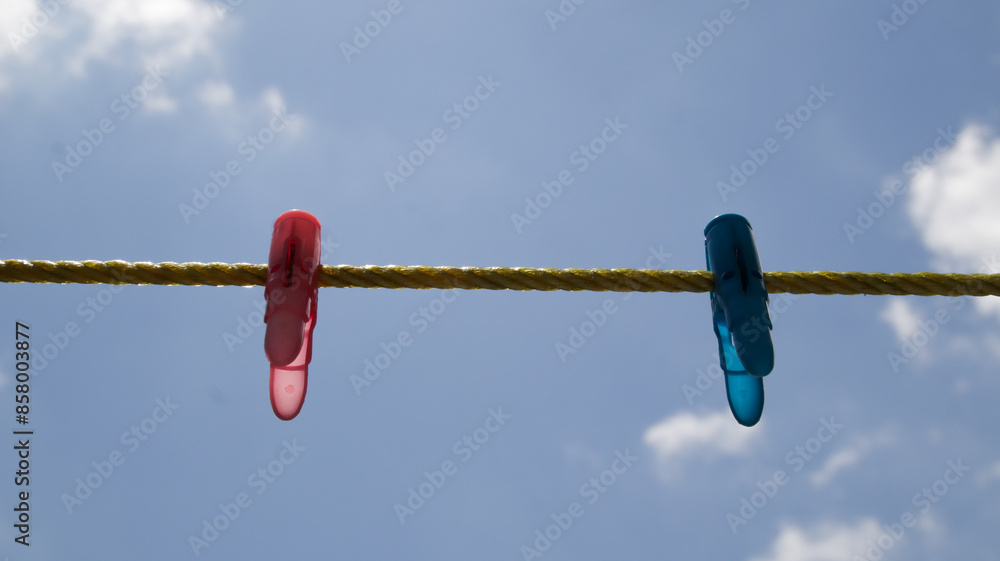 Two Colorful Clothespins on Yellow Rope Against Blue Sky Background in Outdoor Setting Two Colorful Clothespins on Yellow Rope Against Blue Sky Background in Outdoor Setting