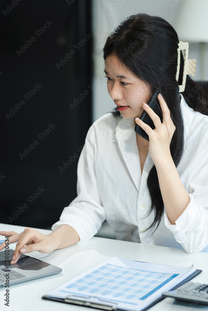 Portrait of Asian businesswoman talking mobile phone and working on laptop and papers on table in her office. Portrait of Asian businesswoman talking mobile phone and working on laptop and papers on table in her office.