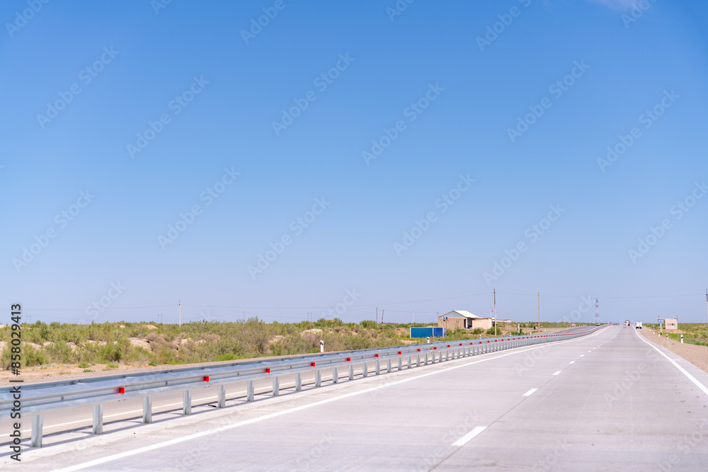 A long, empty highway with a blue sky above. The road is lined with red and white guardrails A long, empty highway with a blue sky above. The road is lined with red and white guardrails