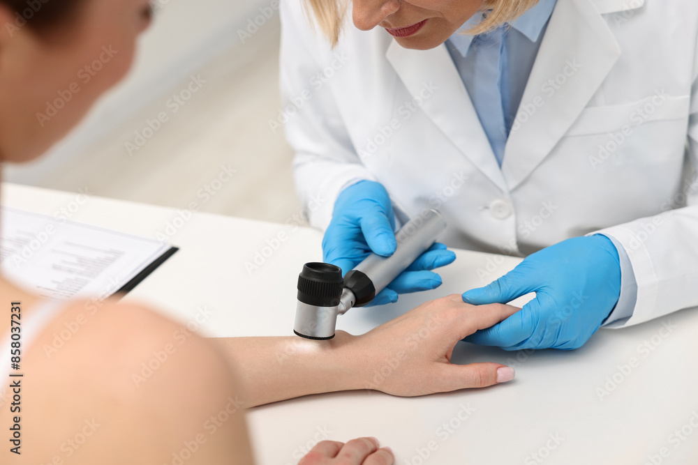 Dermatologist with dermatoscope examining patient at white table in clinic, closeup Dermatologist with dermatoscope examining patient at white table in clinic, closeup