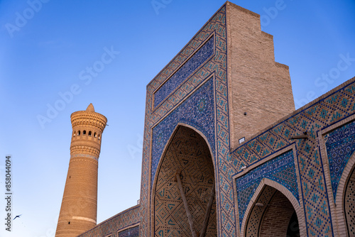 A tall building with a blue archway and a tower in the background. The sky is clear and blue photo