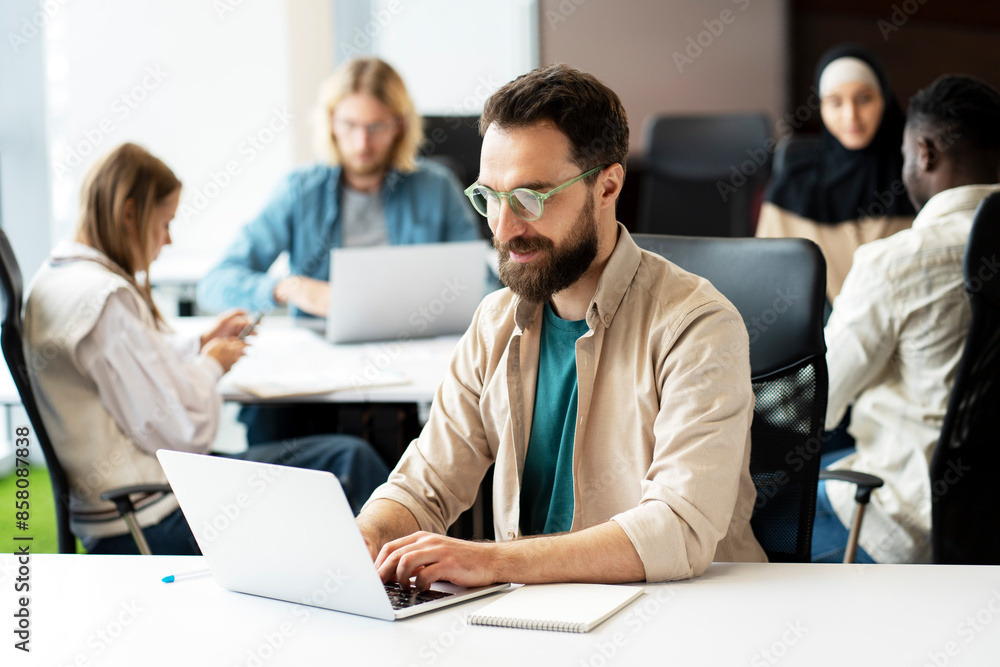 Fototapeta premium Focused bearded man, copywriter typing on keyboard working on laptop in busy office