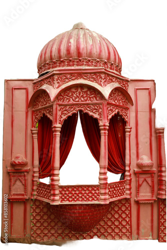 A pink and white building with a red canopy and red curtains. The building has a domed roof and a balcony. The curtains are drawn, revealing a bed inside the building.