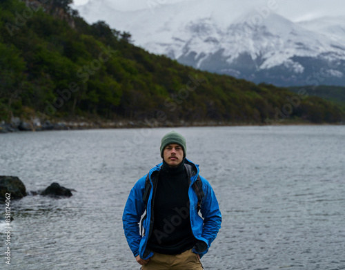 Photo of a handsome young man with mustache, wearing a green woolly hat and blue jacket, posing in front of the Beagle Channel in Tierra del Fuego National Park, Argentina.