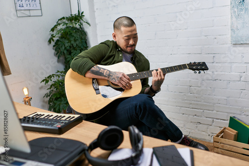 A handsome Asian man plays acoustic guitar in his studio. photo