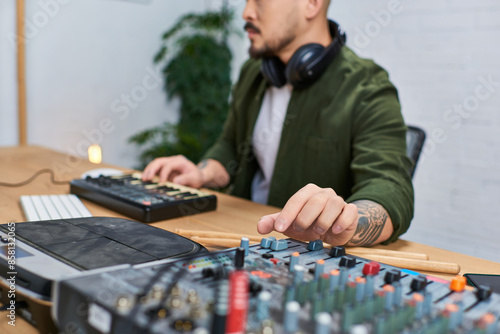 An Asian man sits in his studio, surrounded by musical equipment, focusing on his craft. photo