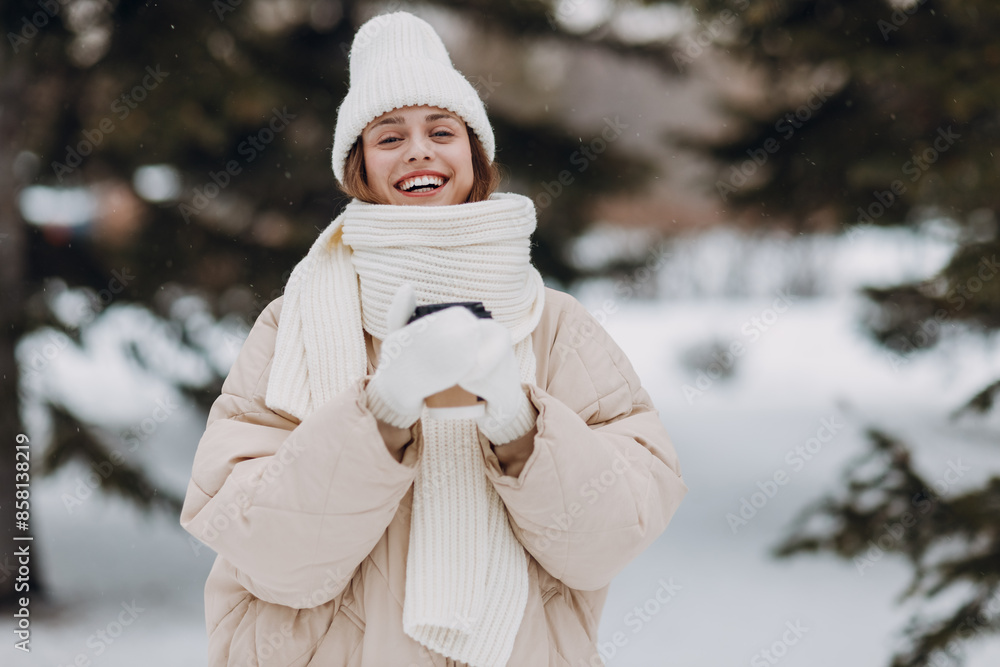 Happy smiling young woman with coffee hot drink cup enjoys winter weather at snowy winter park