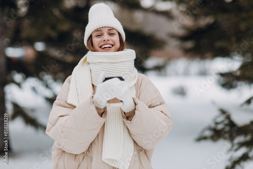 Obraz na płótnie Happy smiling young woman with coffee hot drink cup enjoys winter weather at snowy winter park w salonie