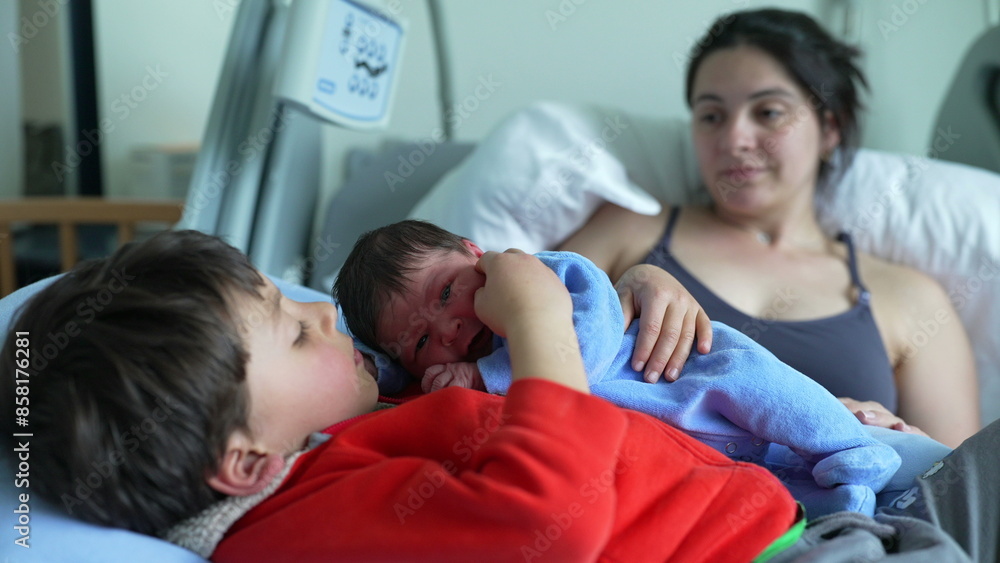 Older sibling lying on hospital bed with newborn baby, while mother watches lovingly in the background. tender family moment of bonding, warmth, and early sibling connection in a hospital setting Older sibling lying on hospital bed with newborn baby, while mother watches lovingly in the background. tender family moment of bonding, warmth, and early sibling connection in a hospital setting