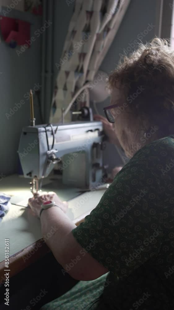 vertical video of an eighty years old woman with sewing experience, preparing the sewing machine to fix a trouser bottom.