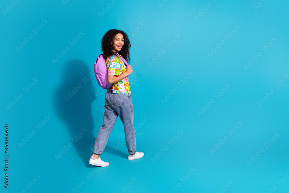 Full length photo of charming good mood girl wear flower print t-shirt rucksack walking empty space isolated blue color background Full length photo of charming good mood girl wear flower print t-shirt rucksack walking empty space isolated blue color background