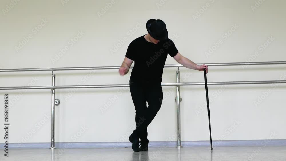 Cabaret or jazz dance with a cane in the studio. A young man in a black gangster hat and black clothes dances driving blues with a stick in his hands Cabaret or jazz dance with a cane in the studio. A young man in a black gangster hat and black clothes dances driving blues with a stick in his hands