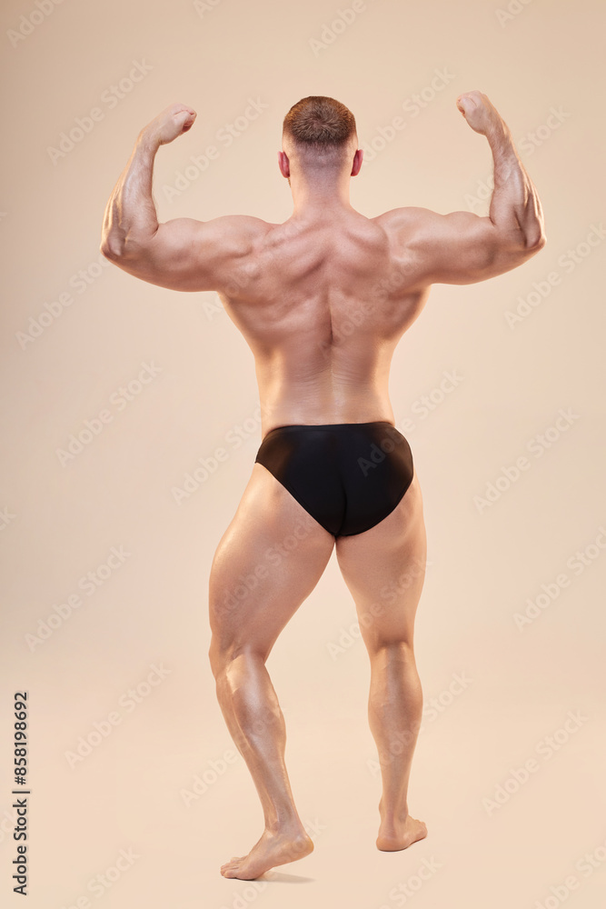 Full shot of young pumped up man showing off musculature in back double biceps pose in studio on neutral background, copy space Full shot of young pumped up man showing off musculature in back double biceps pose in studio on neutral background, copy space