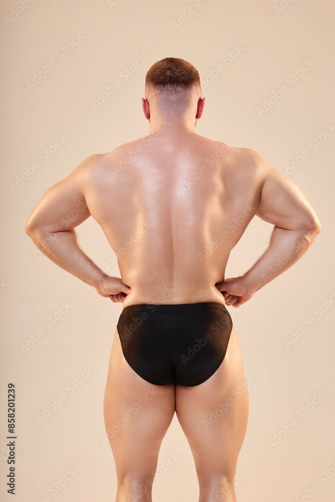 Fototapeta premium Medium full shot of bodybuilders strong back muscles and glowing skin on neutral background. Young pumped up man in rear lat spread pose