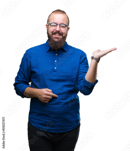 Young caucasian hipster man wearing glasses over isolated background smiling cheerful presenting and pointing with palm of hand looking at the camera.