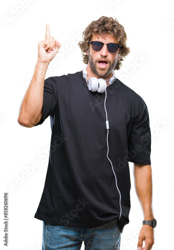 Handsome hispanic man listening to music wearing headphones over isolated background pointing finger up with successful idea. Exited and happy. Number one.