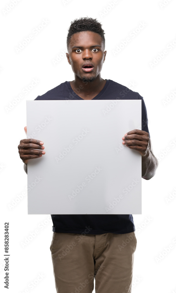 Young african american man holding a banner scared in shock with a surprise face, afraid and excited with fear expression Young african american man holding a banner scared in shock with a surprise face, afraid and excited with fear expression