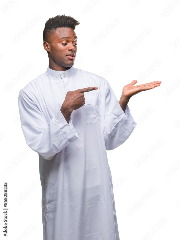 Young arabic african man wearing traditional djellaba over isolated background amazed and smiling to the camera while presenting with hand and pointing with finger. Young arabic african man wearing traditional djellaba over isolated background amazed and smiling to the camera while presenting with hand and pointing with finger.