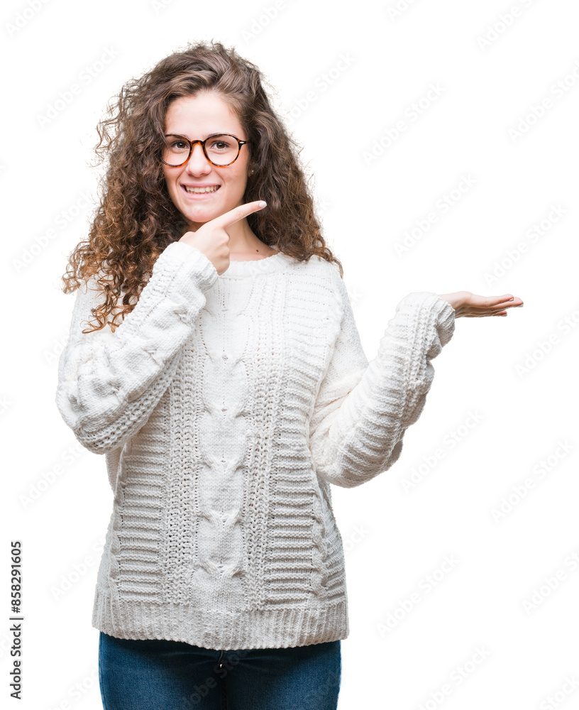 Beautiful brunette curly hair young girl wearing winter sweater over isolated background amazed and smiling to the camera while presenting with hand and pointing with finger. Beautiful brunette curly hair young girl wearing winter sweater over isolated background amazed and smiling to the camera while presenting with hand and pointing with finger.