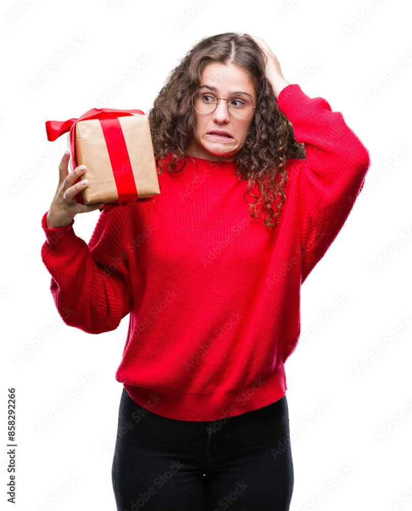 Fototapeta premium Young brunette girl holding a gift over isolated background stressed with hand on head, shocked with shame and surprise face, angry and frustrated. Fear and upset for mistake.